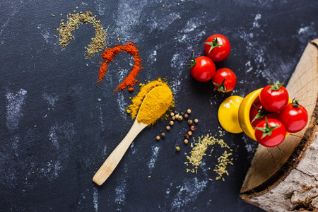 A spoon and spices with cherry tomatoes on a dark tableの写真素材
