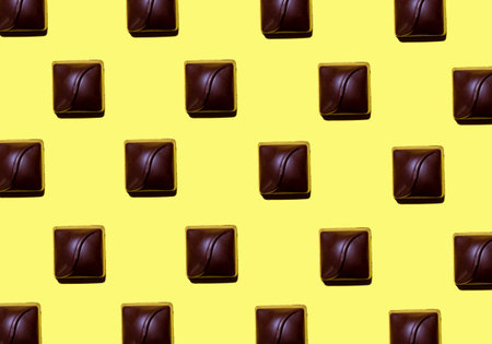 A pastel yellow background with dark square chocolate bonbons pattern - International chocolate dayの写真素材