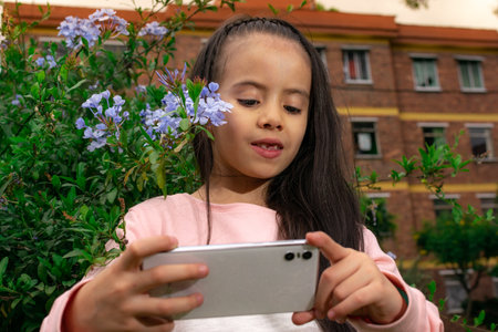 A beautiful Latin American Colombian girl takes a picture next to the flowers of her home garden with her cell phoneの写真素材