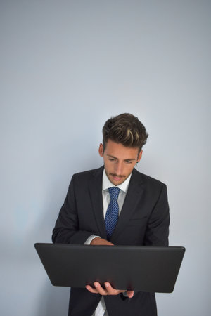 A vertical shot of a Caucasian businessman with a black laptop on the gray wall backgroundの写真素材