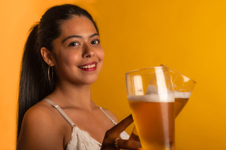 A beautiful Latin female  toasting with beer glass next to a yellow wallの写真素材