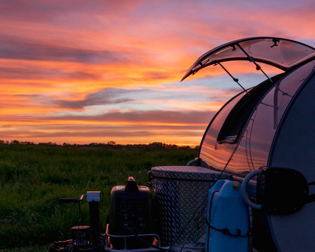 A beautiful shot of a bright colorful sunset on a field with camping equipmentの写真素材