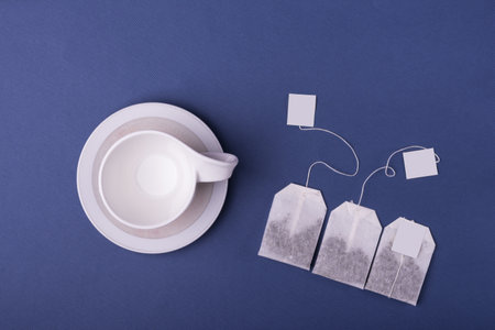 An empty porcelain white cup with three tea bags on blue backgroundの写真素材