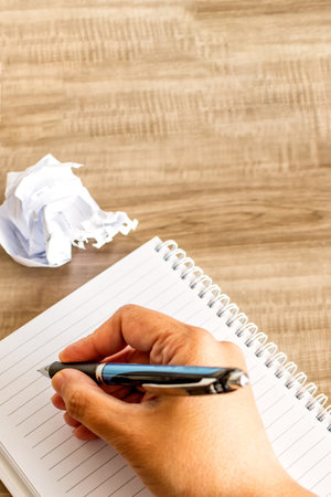 A top view of a female hand writing on a notebook with a pen on a wooden  table