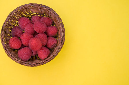 A top view of fresh raspberries in a basket isolated on yellow backgroundの写真素材