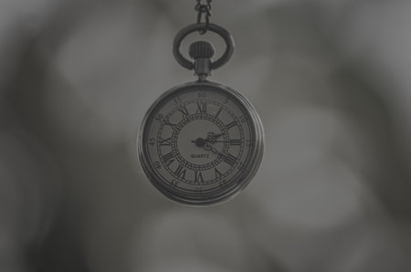 A closeup shot of a retro-style clock on chain on gray background