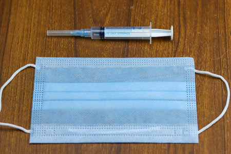A syringe and a face mask on a wooden background - Covid-19 pandemicの写真素材