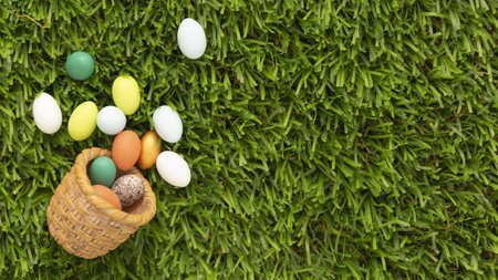 An overhead shot of a toppled wicker basket with colorful Easter eggs on a grassy lawn with space for your textの写真素材