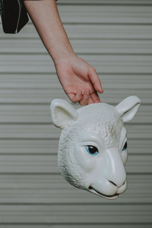 A vertical shot of a female hand holding a sheep maskの写真素材