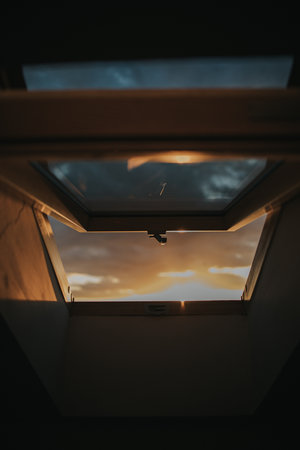 A vertical shot of a half-opened window allowing light from a sunset to creep inの写真素材
