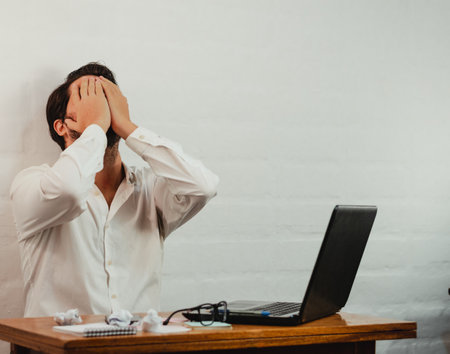 A young Caucasian male with hands on his face showing the gesture of stress and fatigue during workの写真素材
