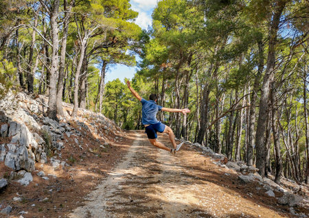 A tourist man happily jumping in the green parkの写真素材