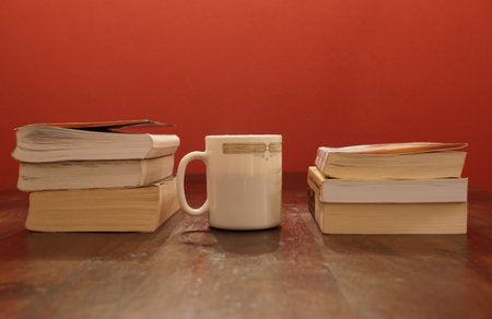 A closeup shot of a coffee cup in the middle of books on the table against a red wall backgroundの写真素材