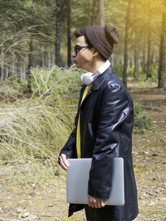A teenager wearing  a cap and sunglasses holding a laptop computer and standing in a parkの写真素材