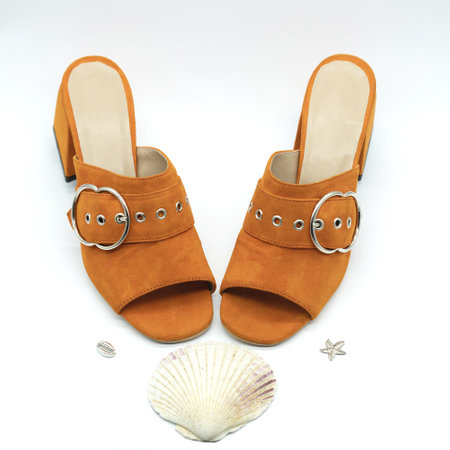A closeup shot of orange sandals on heels with a seashell near i