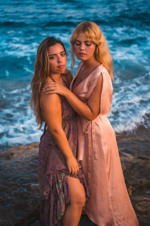 A couple of Caucasian girls posing in pink dresses during summer on the beach by the seaの写真素材