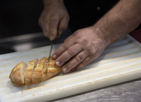A selective focus shot of male hands cutting wheaten bread on the wooden boardの写真素材