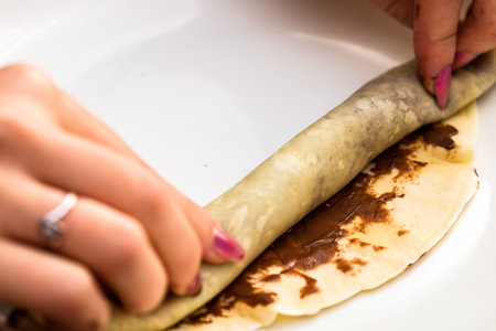 The process of preparing and rolling tasty crepes or pancakes with chocolate creamの写真素材