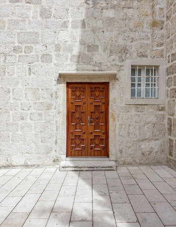 A vertical shot of a decorative brown door and window against a wall buildingの写真素材