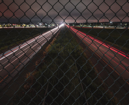 A gorgeous shot of a road from being a metal fence with car headlights showingの写真素材