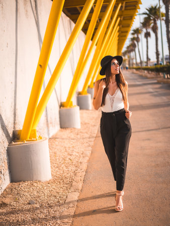 A beautiful brunette female in a black hat walking in a promenade in Torrevieja, Alicante, Spainの写真素材