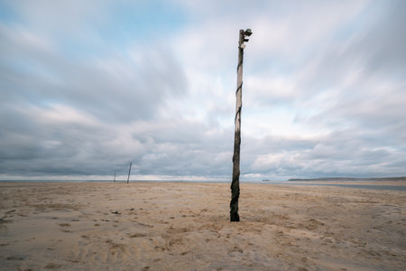A weathered pole on the sandy beach in background of clouds with smooth effectの写真素材