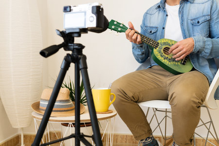 An unrecognizable man recording himself while playing on a green ukulele in a modern studioの写真素材