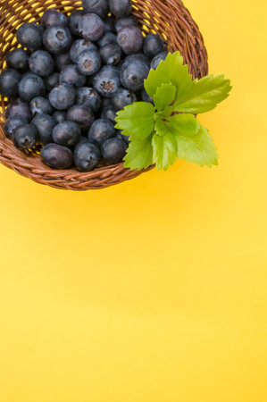 A closeup shot of blueberries in a basket on a yellow backgroundの写真素材