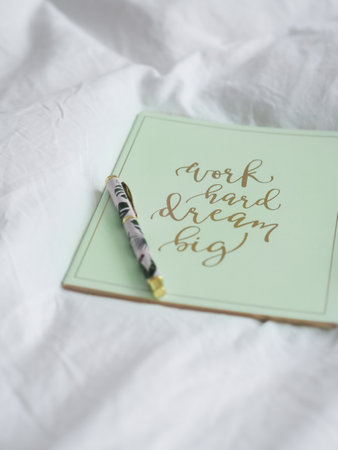 A vertical shot of a green notebook with an inspirational quote on a white cloth with a penの写真素材