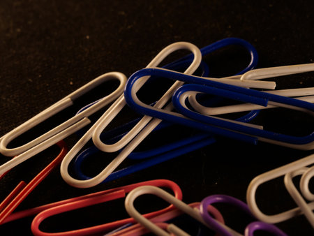 A closeup shot of colorful paperclips on a dark table in the officeの写真素材