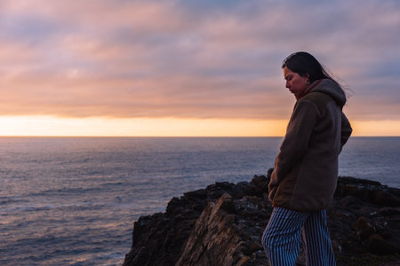 Meditative pensive woman looking at a sunset on the beach, the sun hiding in the sea, day cold Chileの写真素材