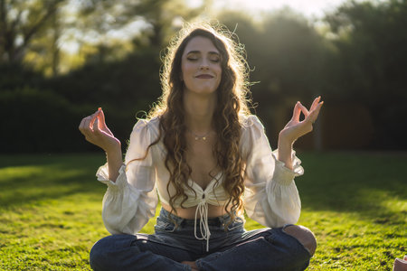 A shallow focus shot of a beautiful Spanish Caucasian woman with curly hair, meditating on the grass and smilingの写真素材
