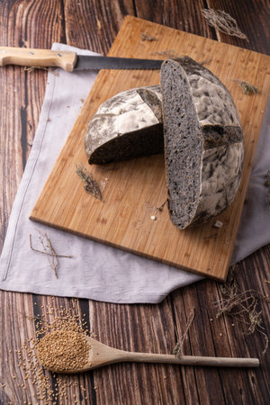 A top view of a Black sourdough bread with sesame seeds on a wooden cutting board on wooden tableの写真素材