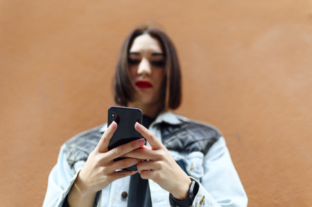 A young stylish Spanish girl texting on the smartphone and posing by the peach color wall; focus on handsの写真素材