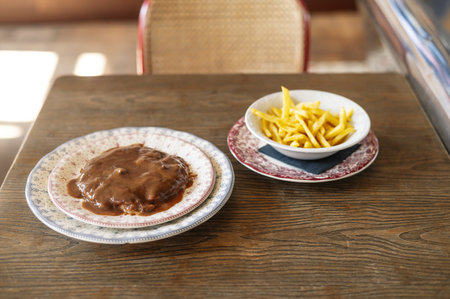An overhead shot of a patty covered with thick savory sauce and a bowl of crispy French friesの写真素材