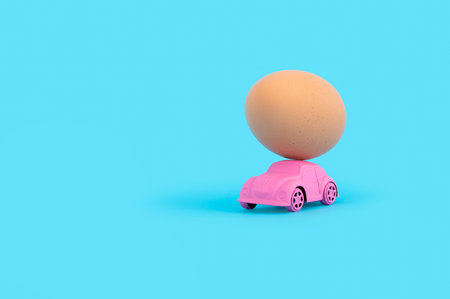 A pink toy car carrying a chicken egg on a blue backgroundの写真素材