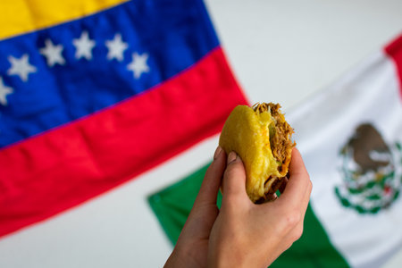 A top view of hands holding cochinita pibil arepa with Mexican and Venezuelan flags on backgroundの写真素材