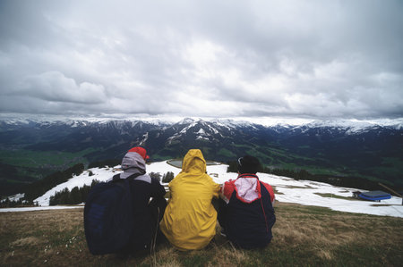 A group of hikers sitting and enjoying the beautiful mountain landscape under a cloudの写真素材