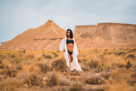A brunette Caucasian model girl in a white dress and a black bikini in a desert one summer afternoonの写真素材