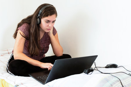 A young Israeli woman sitting in bed, studying or working on her laptopの写真素材