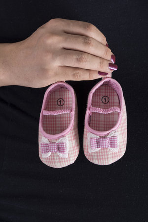 A vertical shot of a woman holding unborn baby girl shoes in hands in front of the bellyの写真素材