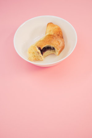 A vertical shot of bitten croissant on a white plate isolated on pink backgroundの写真素材