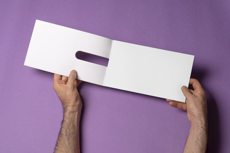 Male hands holding a catalog with blank pages on purple backgroundの写真素材
