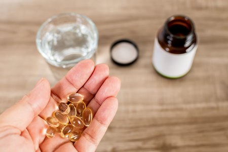 A top view of hands holding pills and glass of water on wooden tableの写真素材