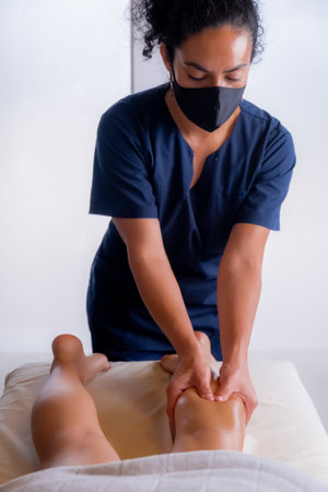 vertical photo masseur giving a leg massage, using a mask, respecting all sanitary regulationsの写真素材
