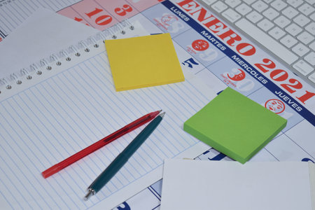 A selective focus shot of notepad, pens, papers, and sticky notes on a calendar in Spanishの写真素材