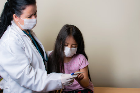 A closeup shot of pediatrician in facial mask examining a little Latin girl in the consulting room - concept of new normalの写真素材