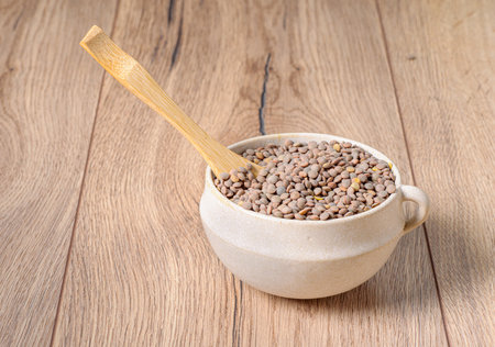 A closeup shot olentils in a clay cup with a wooden spoonの写真素材