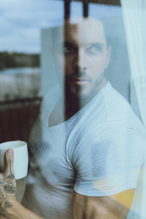A vertical closeup shot of an attractive fit male drinking coffee and looking out the window