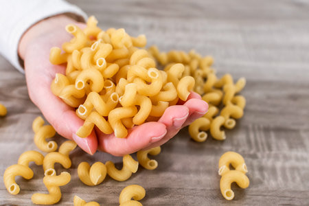 A closeup of a hand holding macaroni on a wooden tableの写真素材
